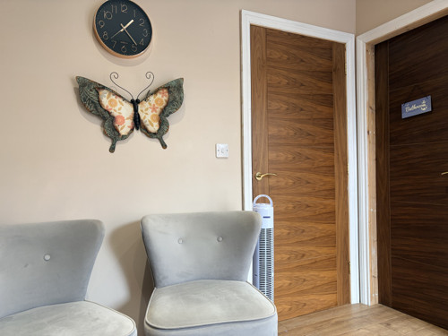 Two soft armchairs in the therapy room, below a wall clock and butterfly wall art